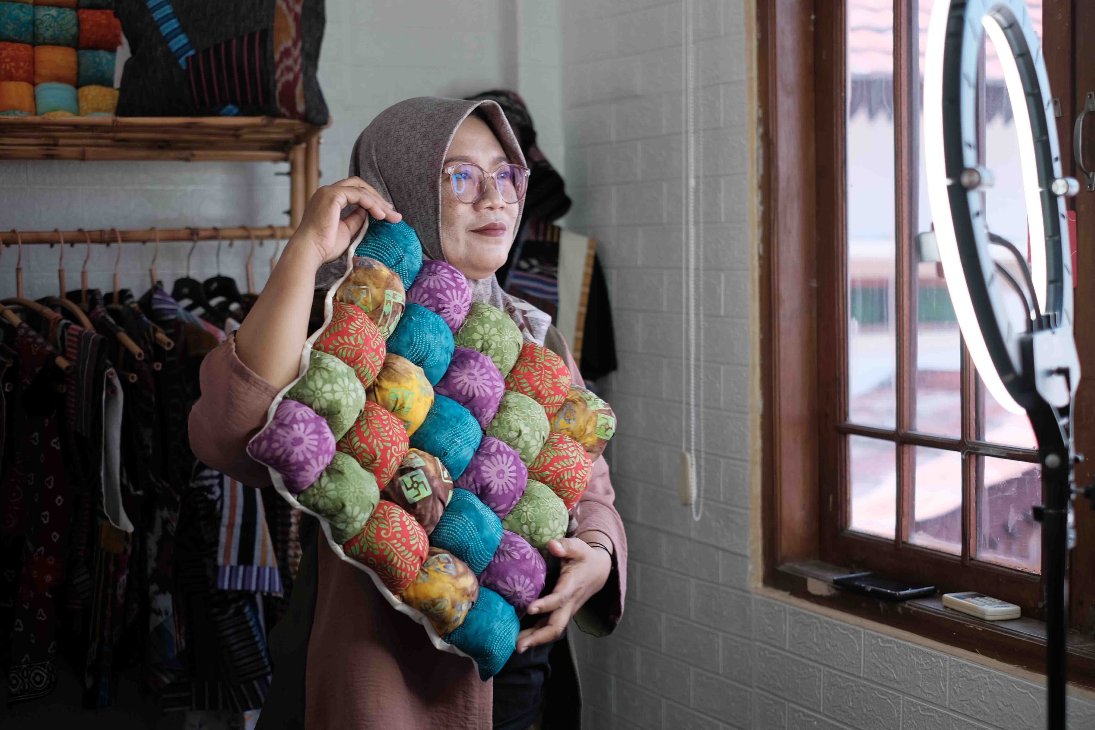 Foto dekoratif menunjukkan salah satu peserta program Diva UMKM sedang mempromosikan produknya berupa bantal dengan motif batik melalui live streaming. 