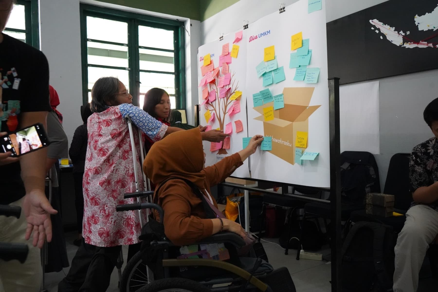 Foto peserta program Diva UMKM dengan disabilitas sedang menempelkan sticky notes berwarna-warni di papan diskusi.