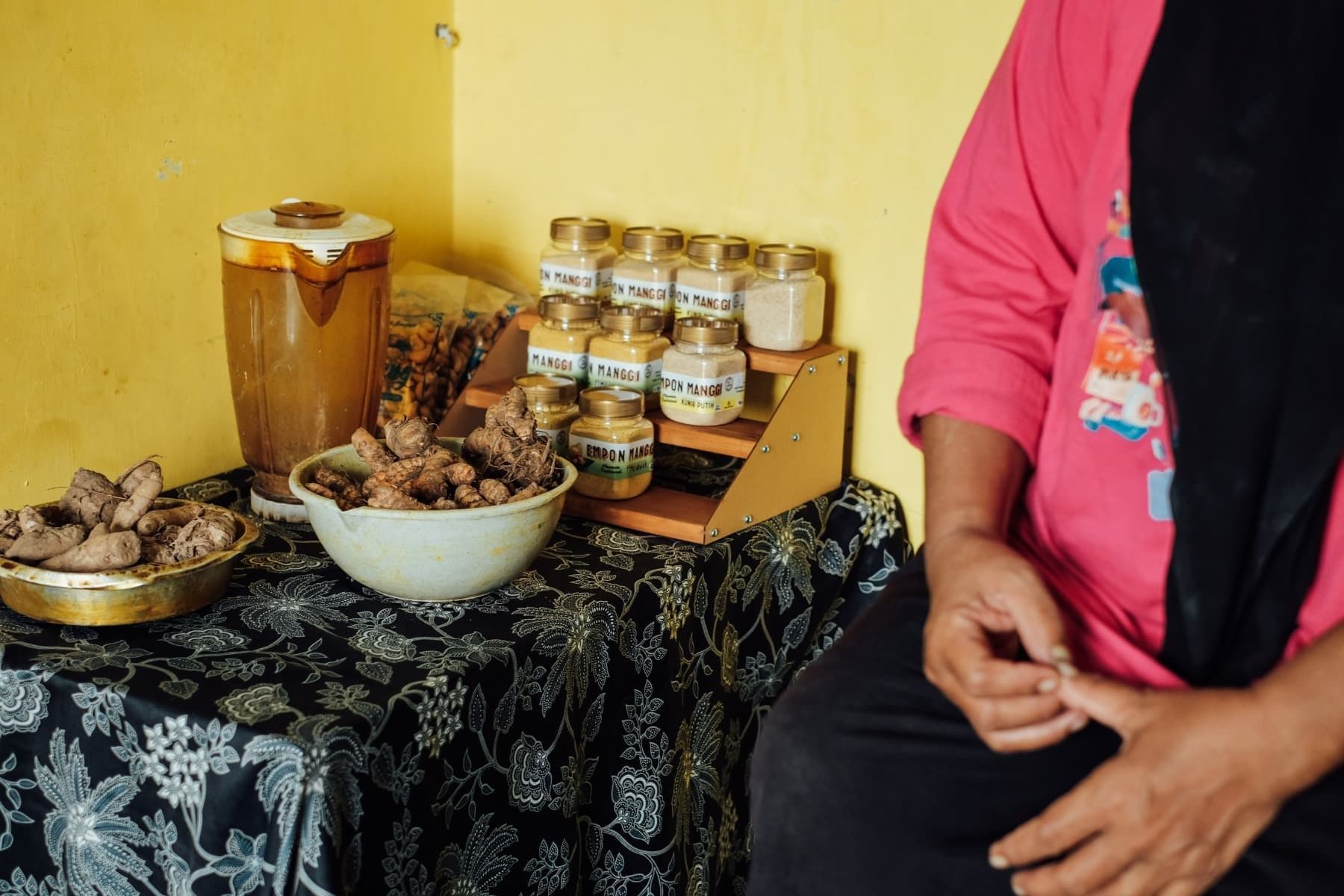 Foto deretan produk jamu instan Empon Manggi dan bahan rempah di meja.