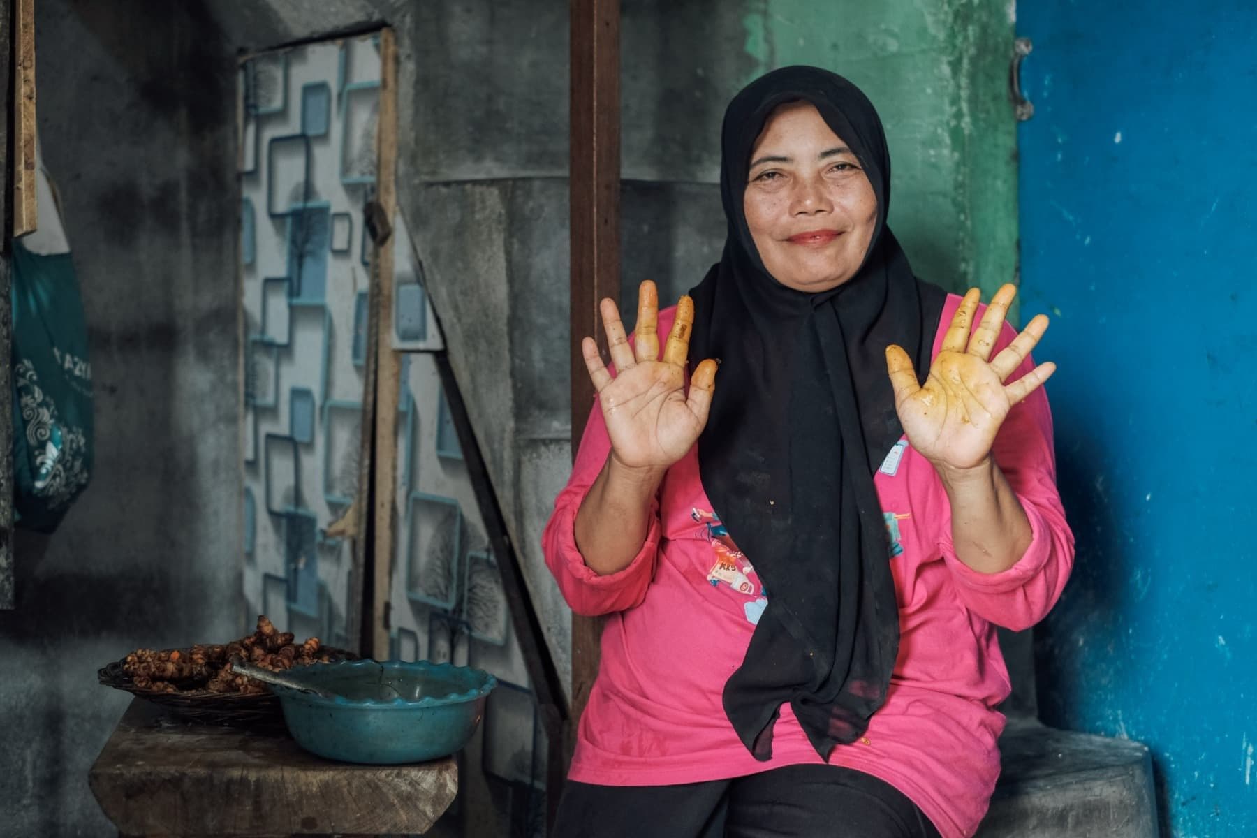 Foto Ibu Warni tersenyum sembari menunjukkan tangannya yang berwarna kuning karena kunyit