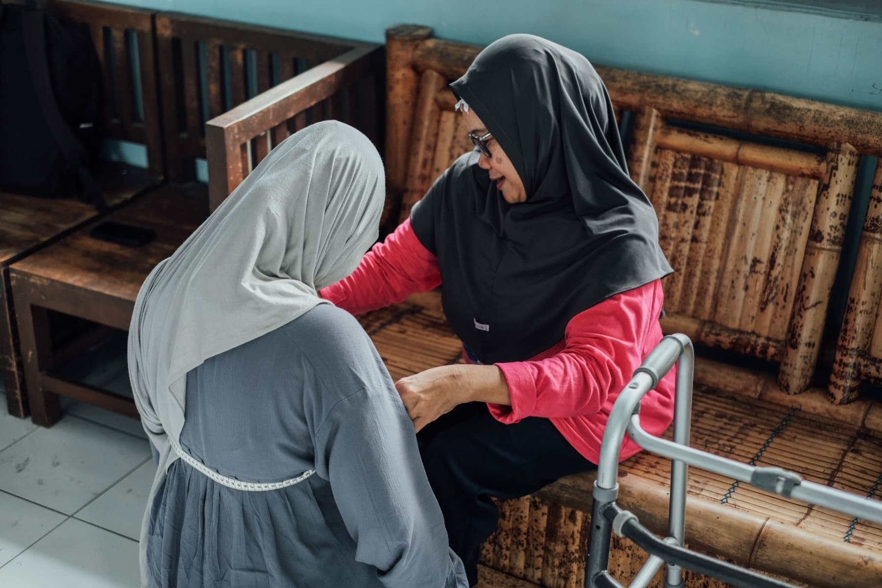 Foto Ibu Endang mengukur pinggang klien dengan meteran jahit sembari terduduk.