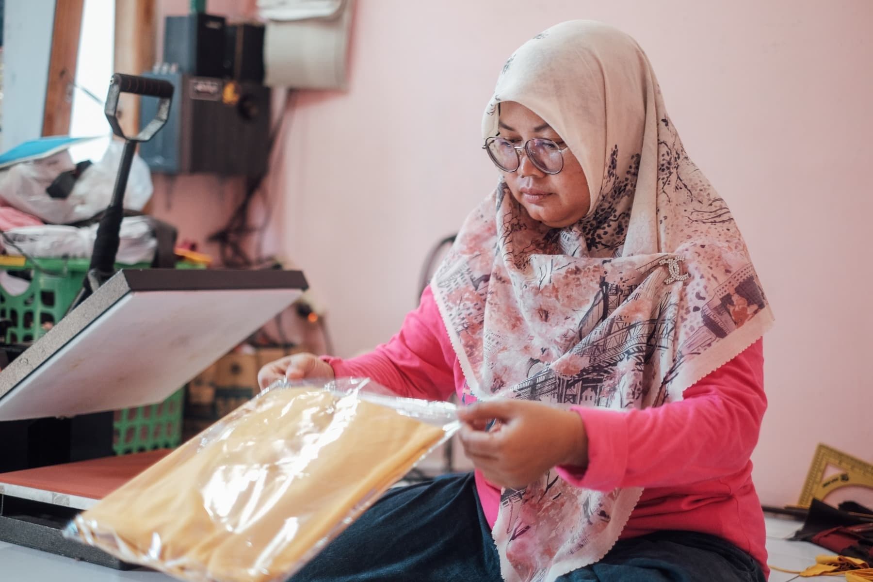 Foto Ibu Rani sedang memasukkan kaos yang telah disablon ke dalam plastik kemasan.