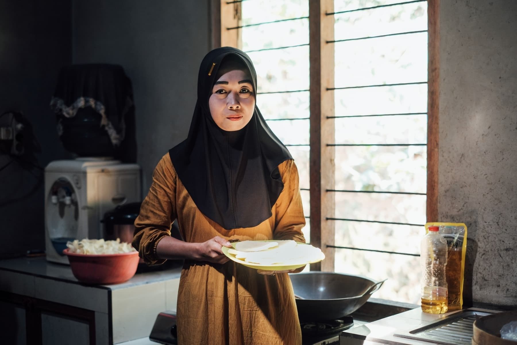 Foto Ibu Dita membawa piring yang berisi lempengan keripik gatot yang akan melalui proses penggorengan.